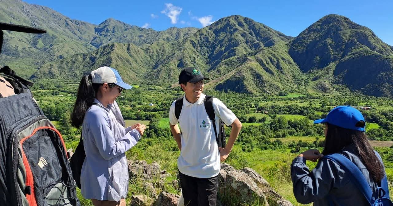 Jóvenes conversando en un cerro con valle verde de fondo